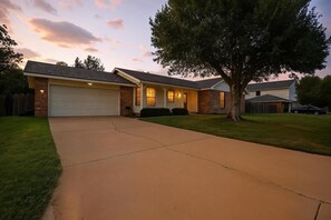 Une maison d’habitation avec un garage, une allée et un grand arbre à l’avant.