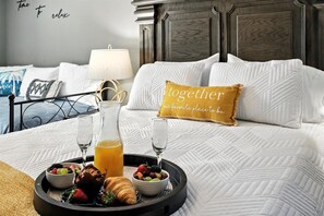 Un lit bien fait, avec un plateau de petit-déjeuner comprenant des croissants, des fruits et du jus, et un oreiller orné de la phrase : « Ensemble, c’est notre endroit préféré. »