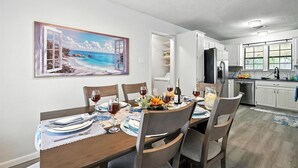 A dining area with a table set for four, a kitchen in the background, and a beach scene painting on the wall. - The Inland Tide 3 bedrooms • 2 bath  • Entire home (Abilene)