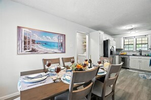 Ein Essbereich mit einem Tisch für vier Personen, eine Küche im Hintergrund und ein Strandbild an der Wand.