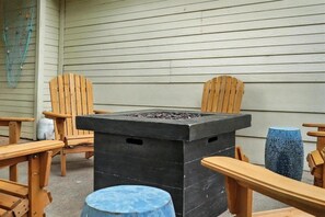 Een terras met een zwarte vuurkorftafel, houten stoelen en een blauwe kruk.
