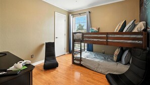 A room with a bunk bed, a desk with a computer and a game controller, a ceiling fan, and a window with curtains. - The Inland Tide 3 bedrooms • 2 bath  • Entire home (Abilene)