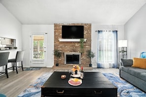 Ein Wohnzimmer mit Kamin, einem darüber montierten Fernseher, einer Couch und einem Couchtisch mit Speisen und Getränken.