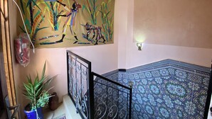 A staircase with a patterned floor, a decorative wall hanging, and a potted plant. - Charming Traditional Apartment – Calm & Cozy, Near Marrakech Airport (Marrakesh)