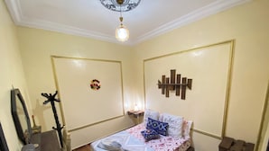 A bedroom with a bed, a nightstand, a mirror, a wall decoration, and a ceiling light. - Charming Traditional Apartment – Calm & Cozy, Near Marrakech Airport (Marrakesh)