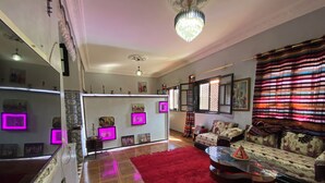 A living room with a red carpet, a sofa set, a glass coffee table, and a chandelier. - Charming Traditional Apartment – Calm & Cozy, Near Marrakech Airport (Marrakesh)