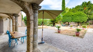 Patio esterno con tavolo e sedie, circondato da colonne in pietra e piante in vaso.