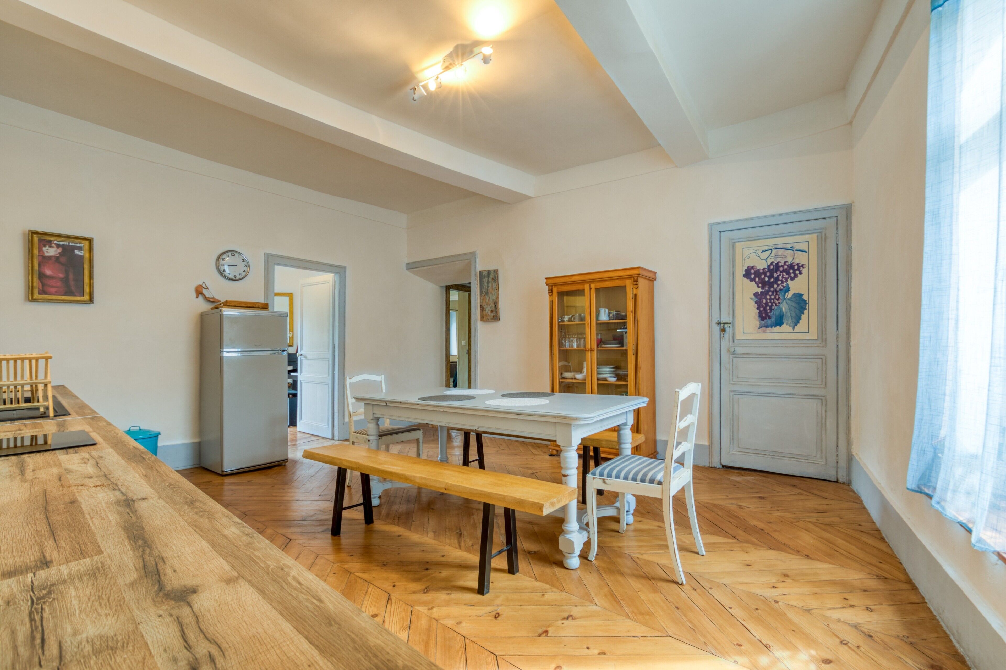 Een keuken met een houten tafel, stoelen, een bankje, een koelkast en een kast.