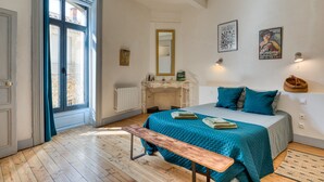 Una camera da letto con un letto, una panca, una cassettiera, uno specchio e un camino.