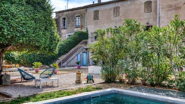 Un espace piscine avec des chaises longues, un escalier menant à un bâtiment et des plantes en pot.