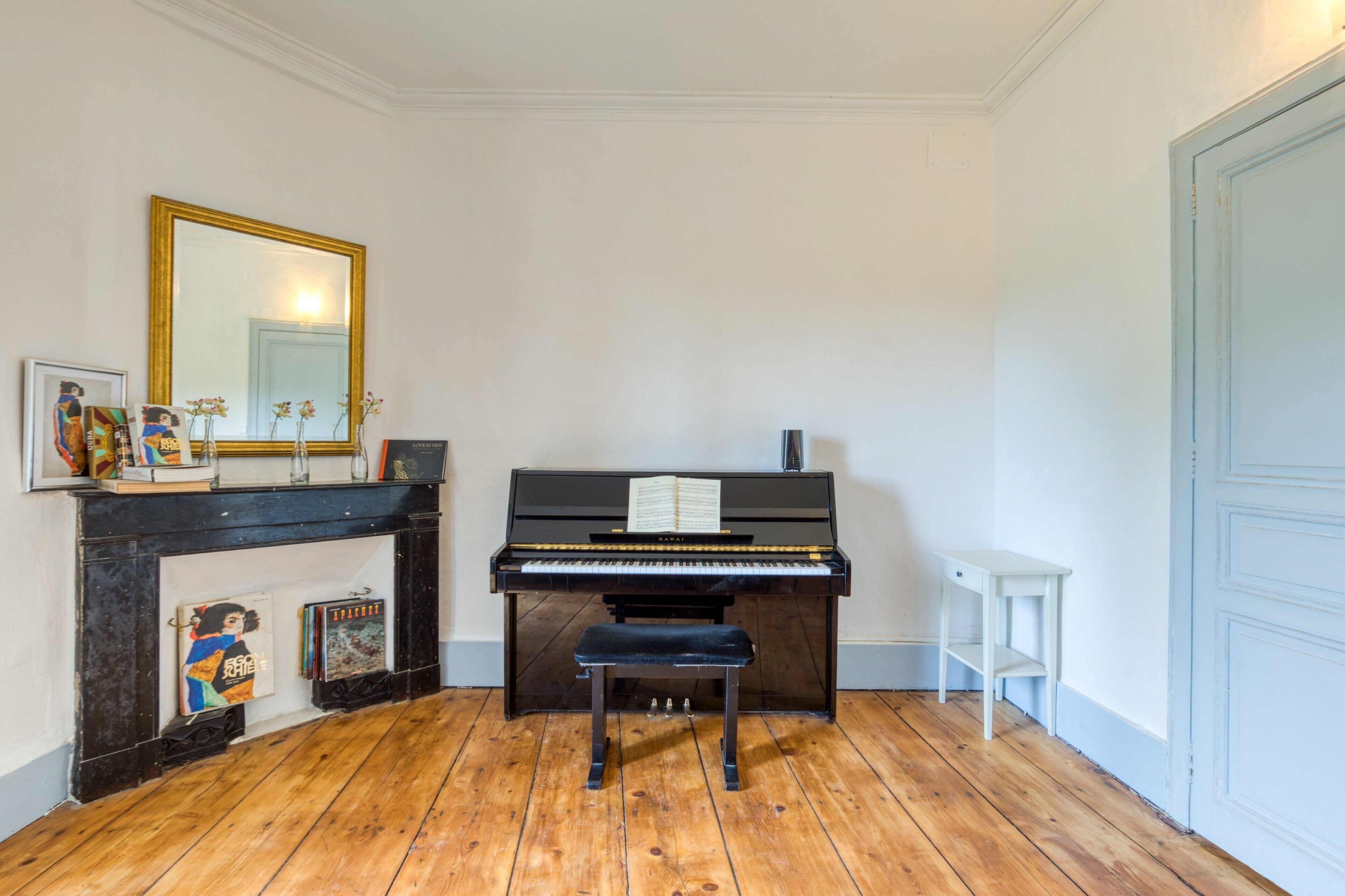 Un piano avec des partitions, un miroir et des livres sur un plancher en bois.