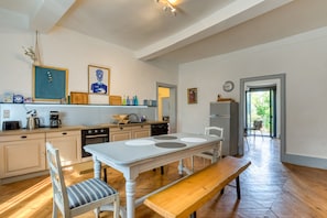 A modern kitchen with a dining table, chairs, a bench, and various kitchen appliances.