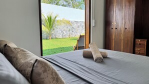 A bedroom with a bed, a wooden wardrobe, and a view of a garden.