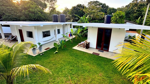 A modern house with a white exterior, a small backyard with grass and potted plants, and a hammock.