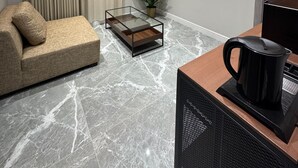 A modern living room with a sofa, a glass coffee table, a potted plant, and a coffee machine.
