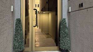 A modern building entrance with a glass door, potted plants, and a security camera above the door.