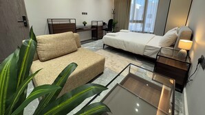 A modern hotel room with a bed, a sofa, a desk, and a large window with curtains.