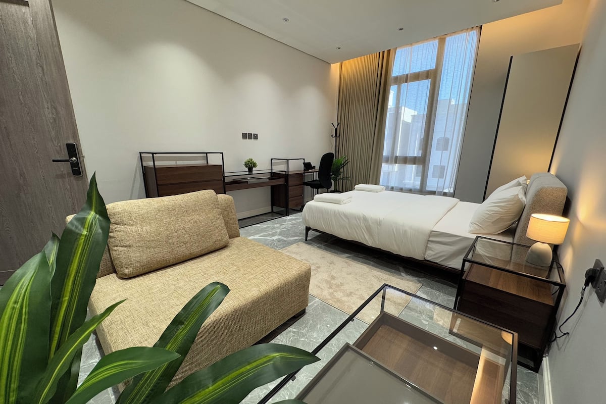 A modern hotel room with a bed, a sofa, a desk, and a large window with curtains.