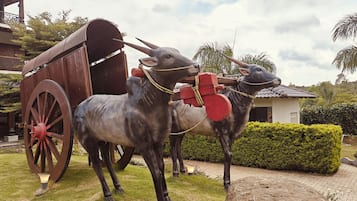Un carruaje de madera tradicional con dos estatuas de bueyes en un jardín ajardinado.