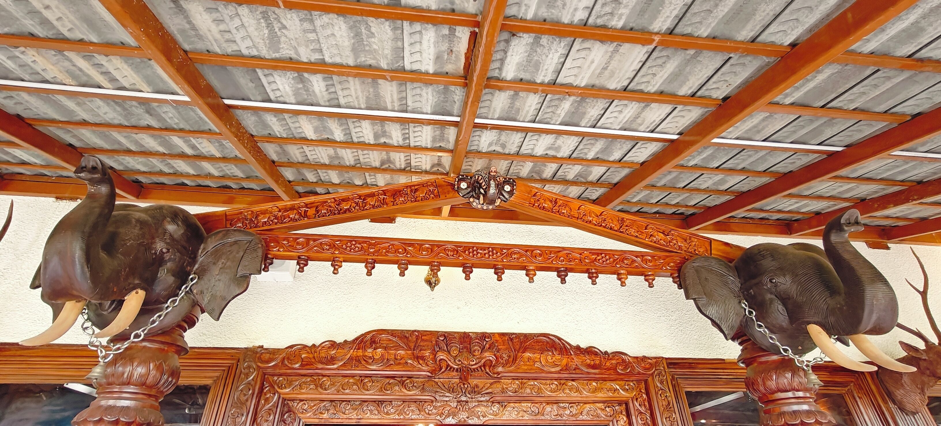 A ceiling with wooden beams and a decorative wooden structure with elephant heads and tusks.