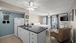 Een compacte hotelkamer met een kitchenette, een bed, een zithoek en een balkon met televisie.