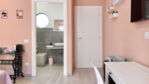 A modern hotel room with a pink wall, a white door, a small table, a white cabinet, a mirror, and a TV mounted on the wall. - La Dolce Cagliari Holiday Home (Cagliari)