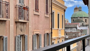 A balcony with a metal railing, overlooking a row of buildings with traditional architecture, including a building with a green dome. - La Dolce Cagliari Holiday Home (Cagliari)