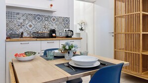 A modern kitchen with a tiled backsplash, a coffee machine, and a dining area with a table set for two. - La Dolce Cagliari Holiday Home (Cagliari)