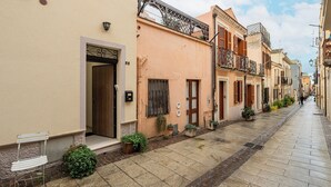 A narrow street lined with buildings, featuring a door with a small bench outside, a window with shutters, and a potted plant. - La Dolce Cagliari Holiday Home (Cagliari)