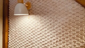 Una habitación con techo texturizado, ventana de madera y lámpara fijada a la pared.
