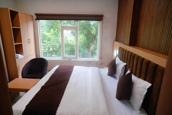 Habitación de hotel con una cama, un escritorio y una silla. Se ve una ventana con vista a árboles.