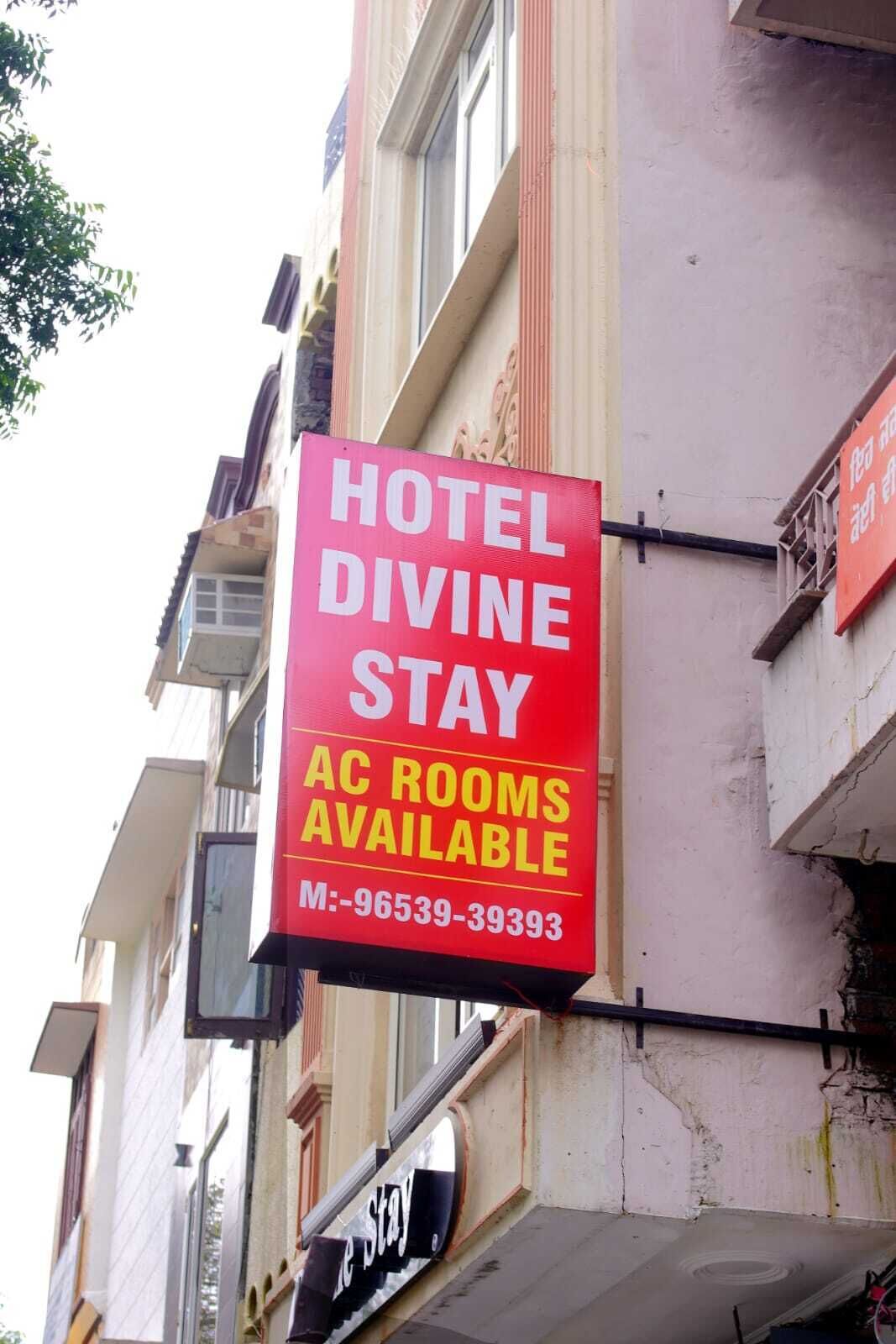 A red sign advertising 'HOTEL DIVINE STAY' with 'AC ROOMS AVAILABLE' and a contact number.