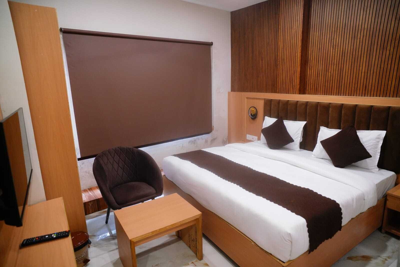Une chambre d’hôtel avec un grand lit, une tête de lit en bois, un petit bureau et une chaise.