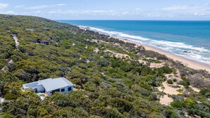 A coastal property with a large house featuring a solar panel roof, surrounded by dense bushland and a beach. - Azumi Yutori Beach House Sunrise (Agnes Water)