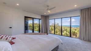 A bedroom with a large bed, a ceiling fan, and a balcony with a view of the ocean. - Azumi Yutori Beach House Sunrise (Agnes Water)