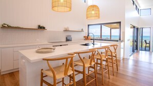 A modern kitchen with a large island, wooden chairs, and pendant lights. - Azumi Yutori Beach House Sunrise (Agnes Water)