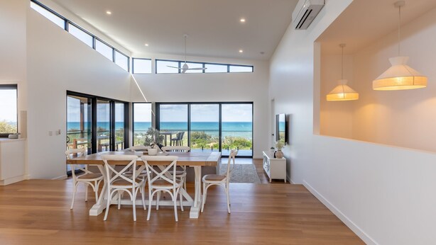 A modern dining area with a view of the ocean, large windows, and a ceiling fan. - Azumi Yutori Beach House Sunrise (Agnes Water)