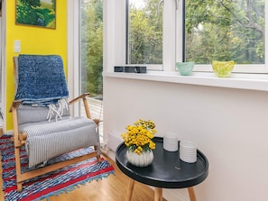 A room with a striped chair, a black table with a vase of yellow flowers, and a window with a view of trees. - 6 Person Holiday Home in Stege (Stege)