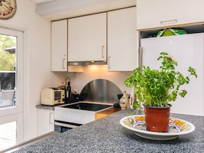 A kitchen with white cabinets, a stainless steel range hood, a potted herb plant on a decorative plate, and a refrigerator with a green item on top. - 6 Person Holiday Home in Stege (Stege)