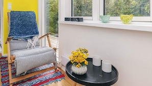 A room with a striped chair, a blue towel, a black table with a vase of yellow flowers, and a window with a view of trees. - 6 Person Holiday Home in Stege (Stege)