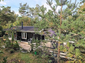 A cabin with a deck, surrounded by dense trees and a clear sky. - 6 Person Holiday Home in Stege (Stege)