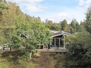 A modern house with a large glass window, surrounded by dense trees and a wooden deck. - 6 Person Holiday Home in Stege (Stege)