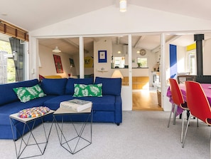 A modern living room with a blue sofa, a coffee table, and a dining area with red chairs. - 6 Person Holiday Home in Stege (Stege)