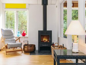 Una sala de estar acogedora con chimenea, un sillón a rayas, una mesa de madera y vistas al exterior.