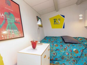 A room with a bed, a small white cabinet, a poster on the wall, and a lamp.