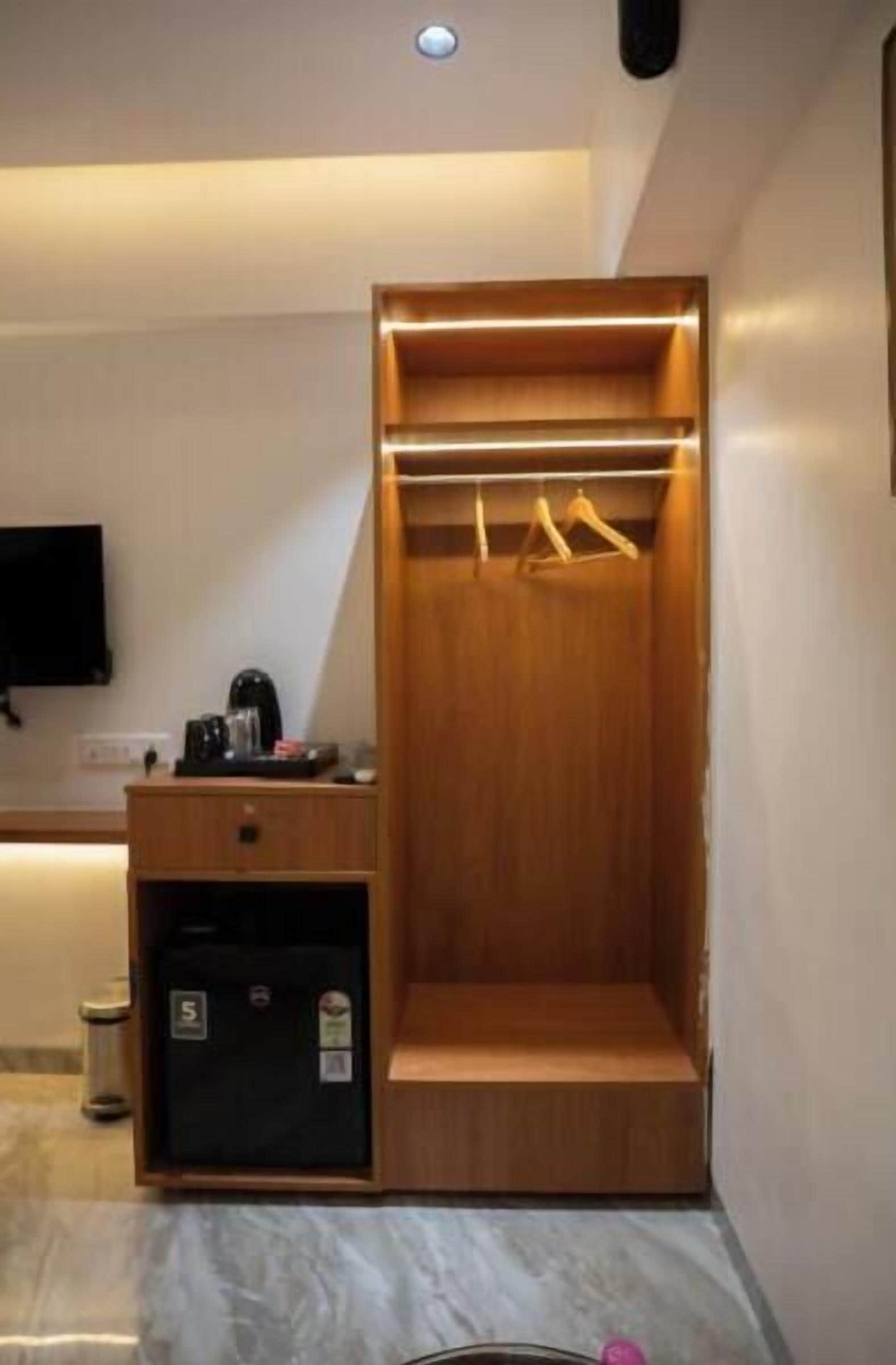 A compact room with a built-in wardrobe, a small desk with a coffee maker, and a television mounted on the wall.