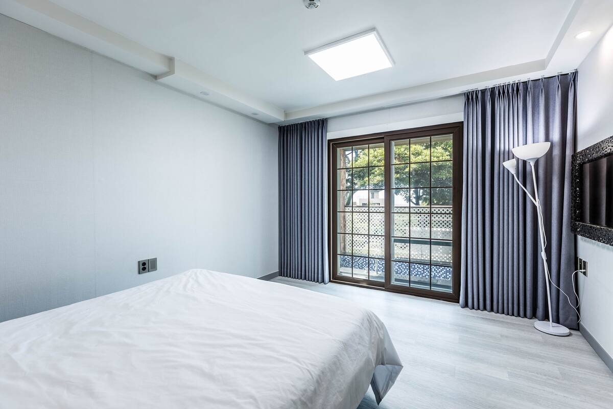 Una habitación de hotel con una cama, una lámpara de pie y un ventanal con cortinas.