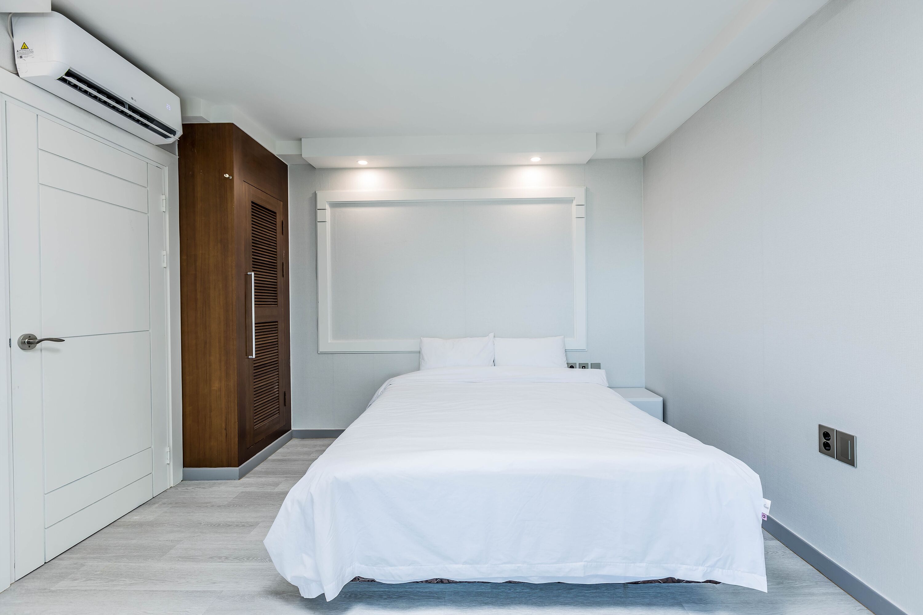 A modern bedroom with a large bed, a wardrobe, and an air conditioning unit.
