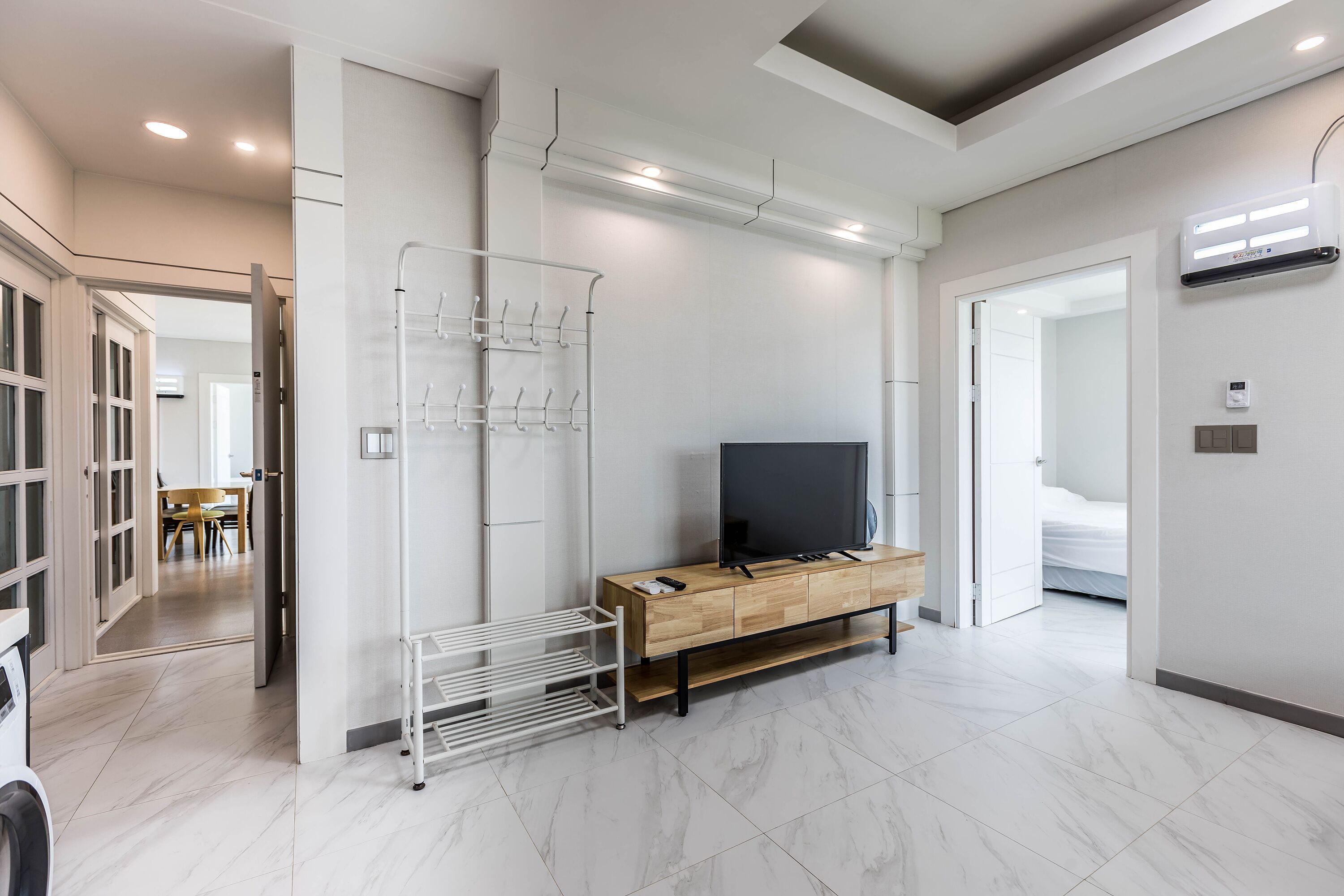 Una camera d'hotel moderna con un armadietto in legno, una TV a schermo piatto, un portascopino bianco e un corridoio che conduce a un'altra stanza.