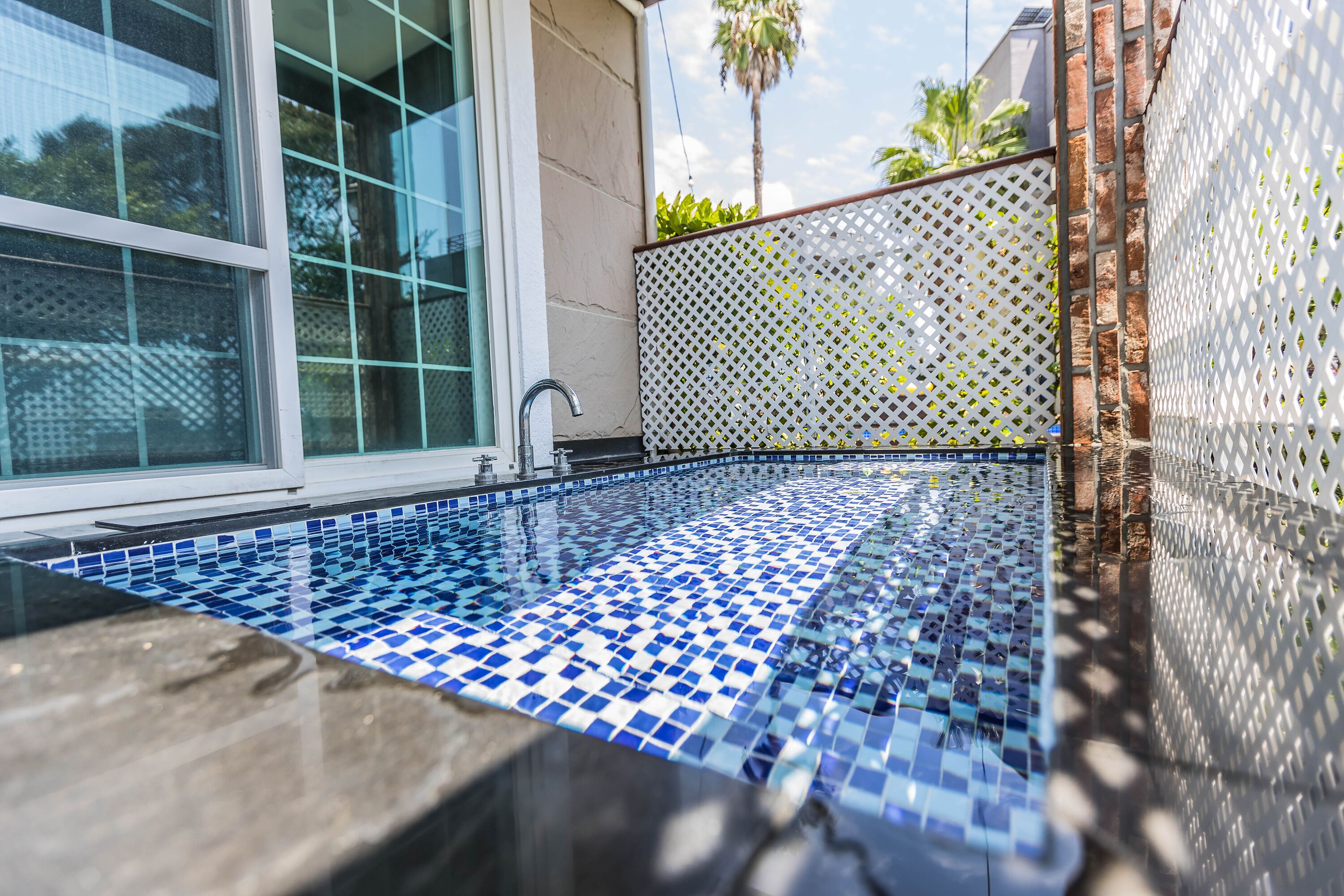 Ein Swimmingpool mit blauen und weißen Mosaikfliesen, einem Metallarmaturen und einem weißen Gitterzaun.